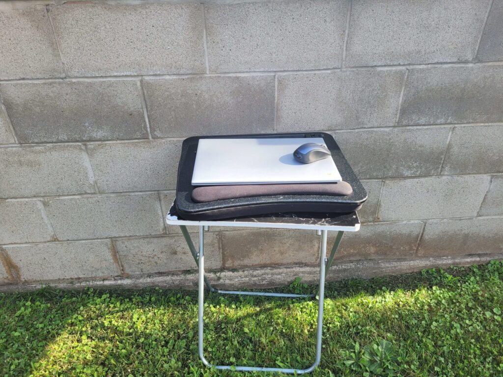 Laptop and Mouse on a folding desk against a brick wall outdoors
