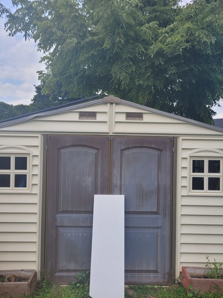 Styrofoam insulation sheet leaning on a resin shed representing one of the cheapest ways to insulate a shed office