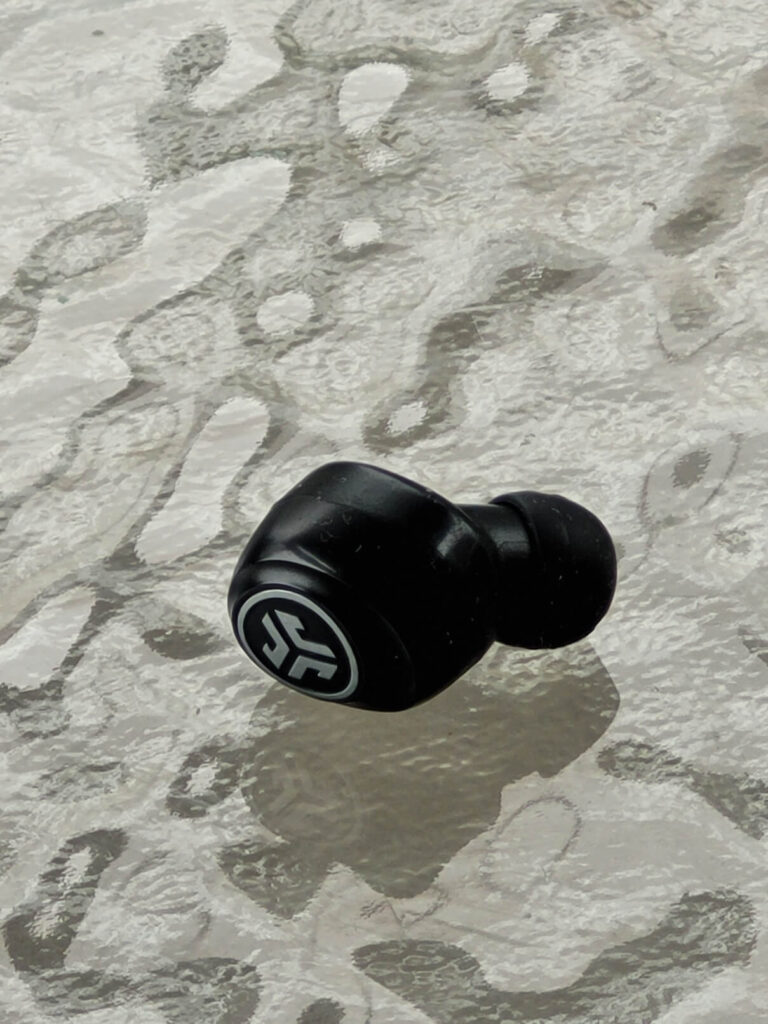 Closeup of a single earbud sitting on a frosted glass table