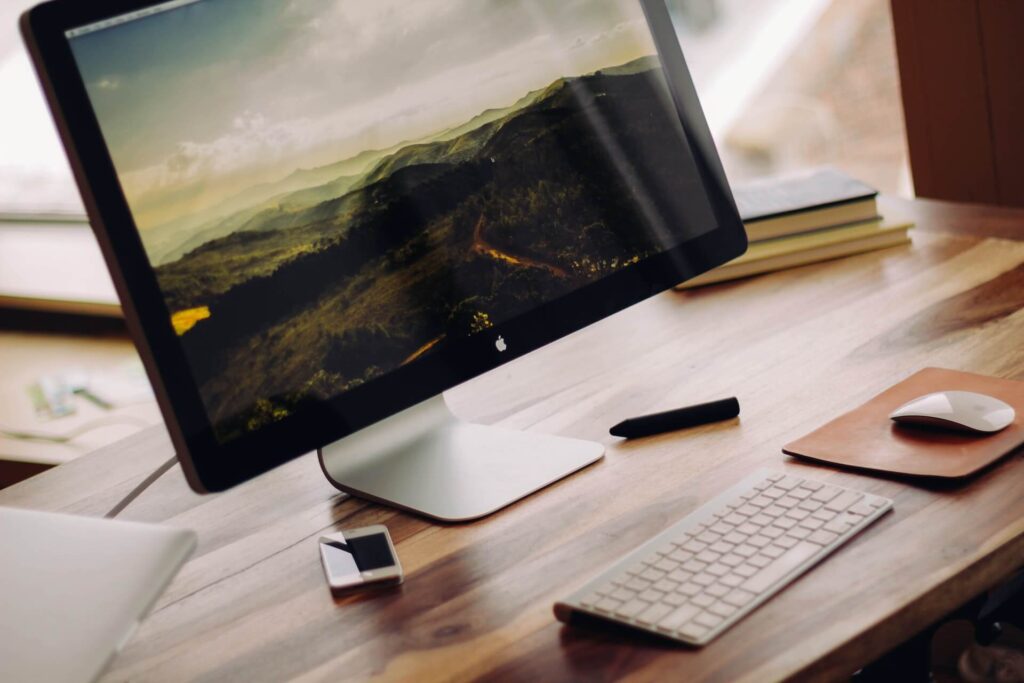 Small desk with monitor, keyboard, mouse and smartphone on the surface