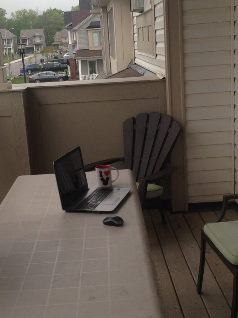 A clutter free outdoor desk with a laptop, coffee cup and mouse