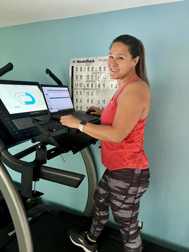 A happy Walk-i-Task customer on her treadmill typing on her laptop using the treadmill desktop attachment