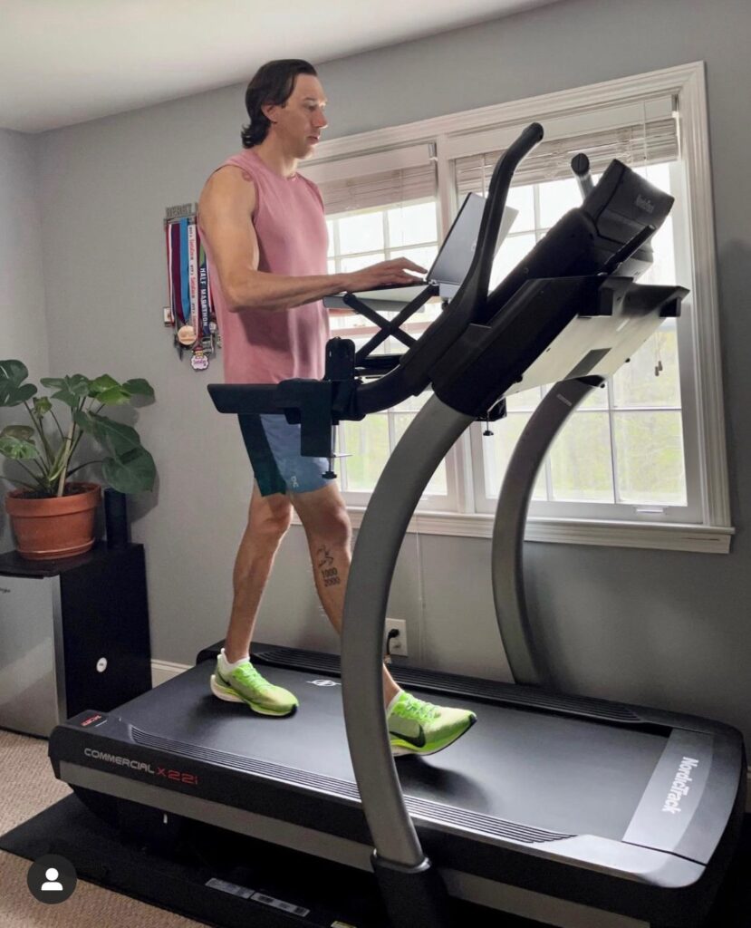 Man walking on treadmill while typing on laptop sitting on Wak-i-Task desk attachment in bright and airy room