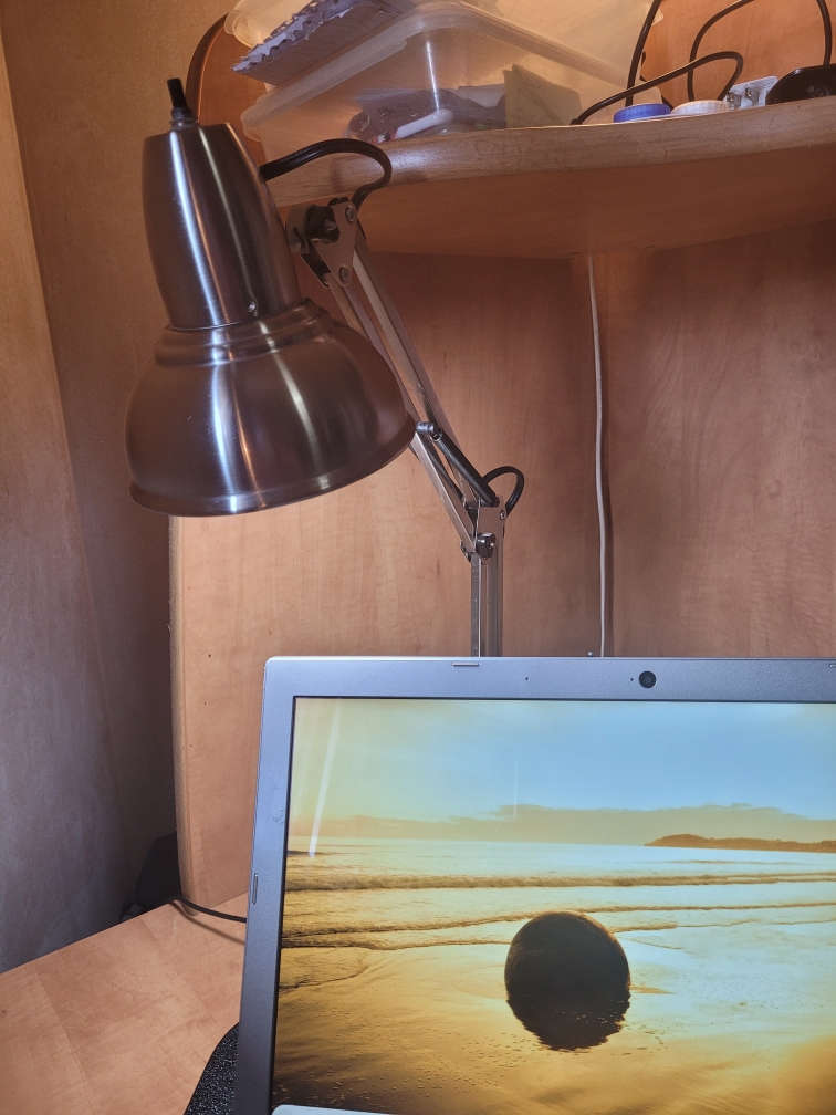 A closeup pic of a laptop on a desk with a lamp overtop of the computer.

