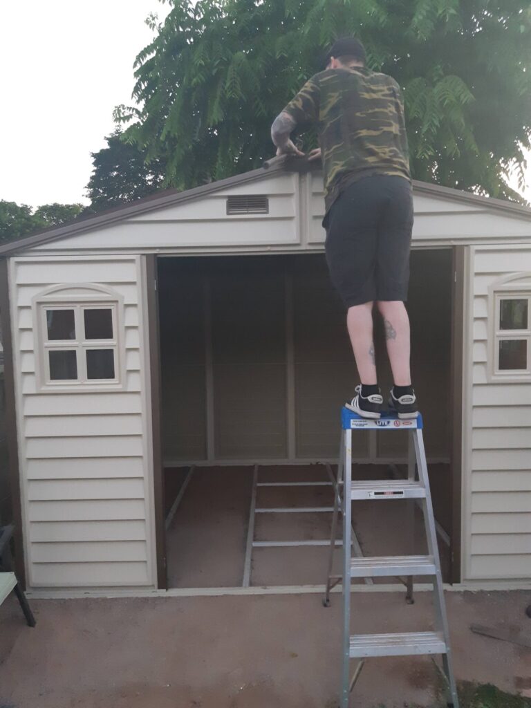 A shed build nearly completed with a man on a ladder adding the finishing touches as an example of how to find the best contractor for your new backyard office.